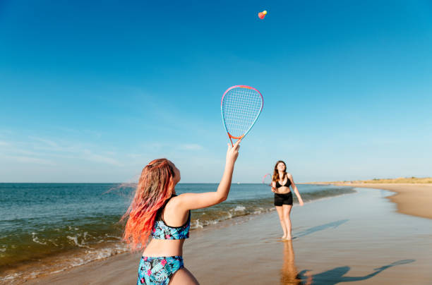 The photograph captures two young boys joyfully playing soccer on the beach. Their laughter fills the air as they chase the ball across the soft, sandy surface, their bare feet kicking up clouds of sand with each stride. The sun casts a warm glow, illuminating their bright swim trunks and adding a cheerful ambiance to the scene.