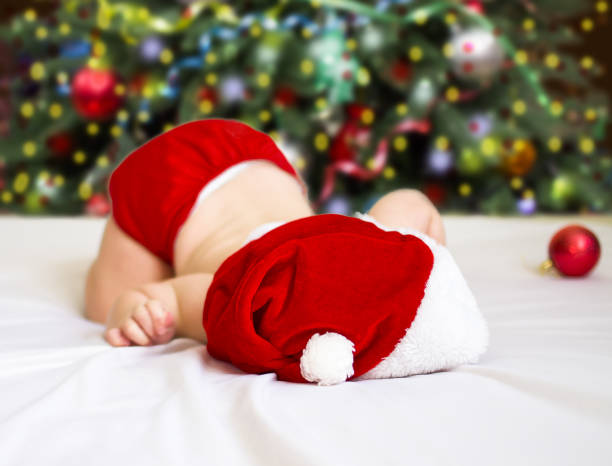 un neonato in un cappello di babbo natale giace sul letto con il sedere sollevato - baby santa claus christmas sleeping foto e immagini stock