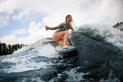 cheerful woman rides down the wave sitting on a wakeboard. Wakesurfing on the river. Summertime leisure