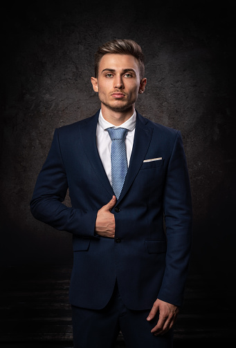 Conceptual portrait of a young, stylish business man, in a blue suit and tie, against a dark textured background. High quality photo