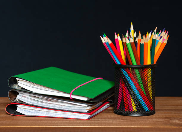 istock Wooden multi-colored pencils and a stack of paper notebooks on a dark background. Stationery 1345215319