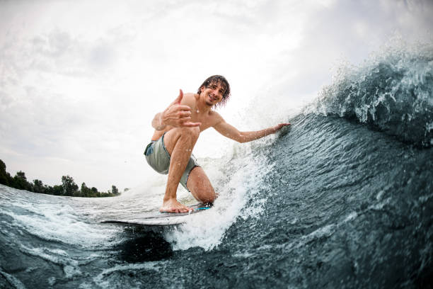 istock man show hand gesture riding on surf style wakeboard and touching the wave with one hand 1345216412