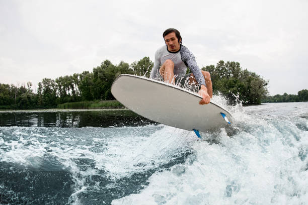 istock Energetic guy with wakesurf board fly over splashing river wave. 1345217243