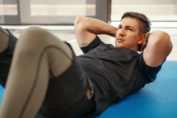 Young muscular caucasian handsome man doing abs exercises on a mat