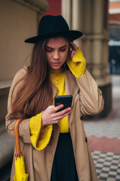 istock Young beautiful woman using a smartphone and holding a yellow umbrella 1345218041