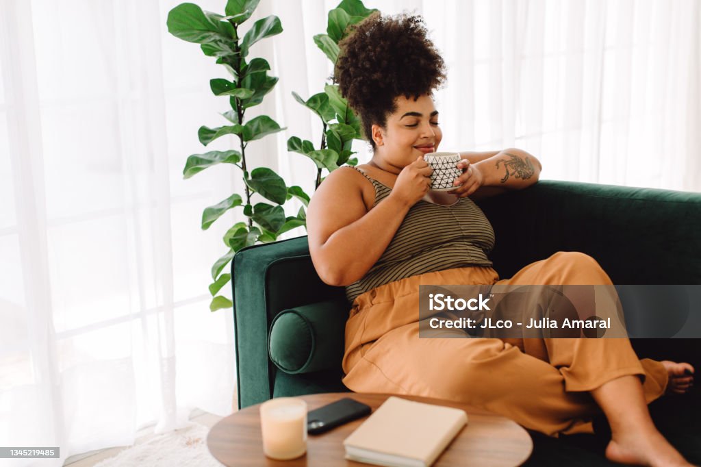 Healthy woman having coffee at home Beautiful female having coffee at home. Woman relaxing on sofa and having coffee. Relaxation Stock Photo