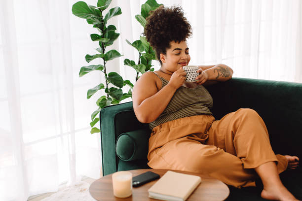 Healthy woman having coffee at home Beautiful female having coffee at home. Woman relaxing on sofa and having coffee. plus size stock pictures, royalty-free photos & images