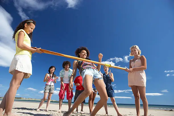 Group Of Teenagers doing limbo dance on beach