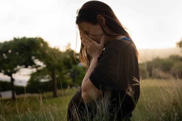 A stressed unhappy pregnant woman sitting alone covering her face. Prenatal depression. A sad pregnant woman sitting outside on the grass crying in tears covering her face. relationship difficulties photos stock pictures, royalty-free photos & images