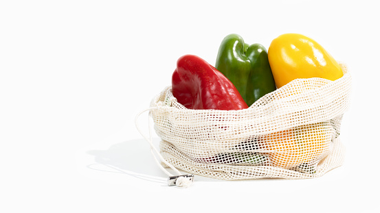 Ripe yellow, green and red bell pepper lies in a fabric net string bag. Ecology concept, zero waste, no plastic. Shopping local seasonal vegetables.