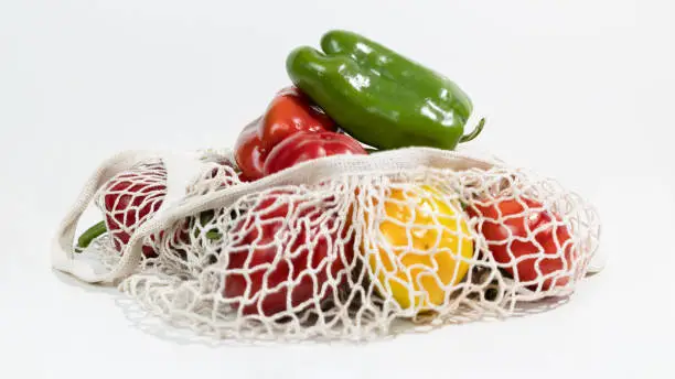 Photo of Ripe yellow, green and red bell pepper lies in a fabric net string bag. Shopping local seasonal vegetables.