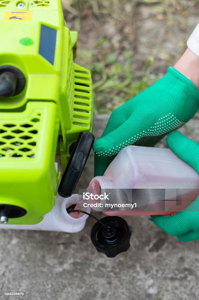 Refuel the mower with gasoline from can Hands in gloves filling the grass cutter mower with gasoline petrol from plastic can Adult Stock Photo