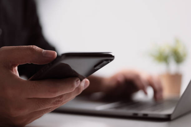 istock Businessman hand using a smartphone and reading messages via an app while working on a laptop computer at a desk in the workplace. 1345233392