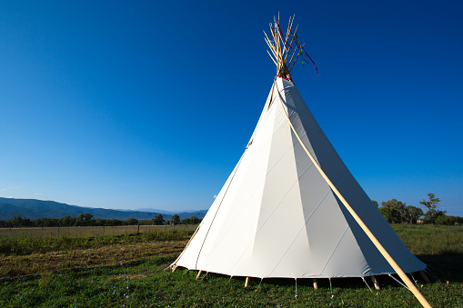 White tipi or teepee in the foreground with a former buffalo jump in the background. Photographed at the First Peoples Buffalo Jump State Park in Montana.