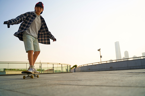 teenage asian child skateboarding outdoors on a pedestrian bridge