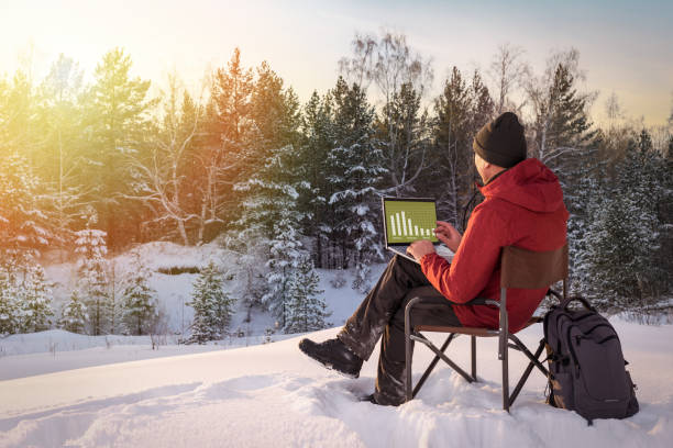 istock Man working on laptop in forest covered with snow at sunset. Concept remote work. 1345241457