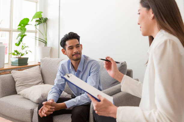 Young Asian man talking his problems with professional psychologist while conducting a consultation and making notes to seek advice and therapy