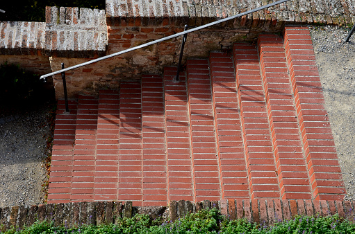 park staircase on the terrace of an Italian garden. the stairs are made of red bricks glued to cement. forged metal railing on the retaining wall, faassenii, nepeta,
