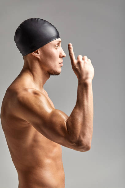 junger profi-schwimmer mann zeigt mit den fingern nach oben einen leeren raum - bademütze stock-fotos und bilder