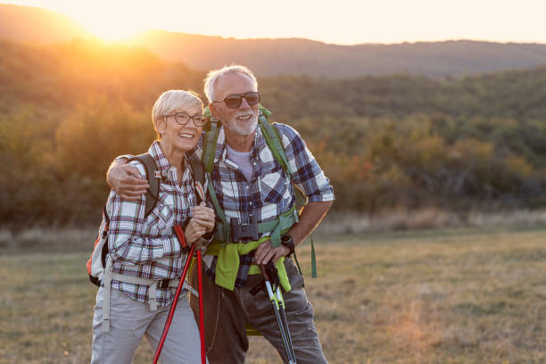 coppia di persone mature sorridono e riposano dopo aver camminato nella natura con il tramonto sullo sfondo - hiking mature adult women senior adult foto e immagini stock