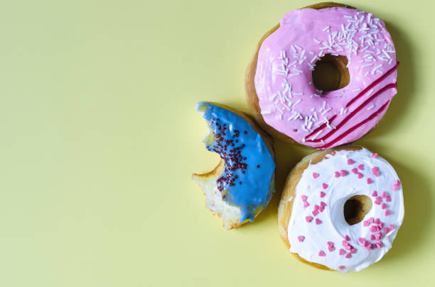 istock Donuts with colored glaze on a yellow background of the copy space. Colored donuts and a half-eaten donut on a colored flat lei background 1345256753