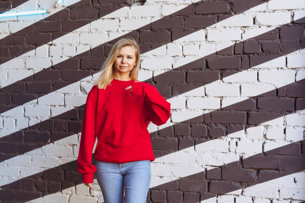 Woman in a red sweatshirt stands against a black and white roller wall.