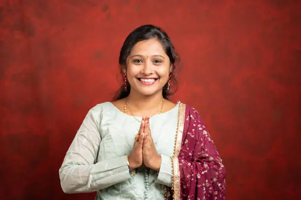 happy smiling Indian girl with traditional ethnic dress in namaste gesture looking at camera - concept of Indian way of greeting.