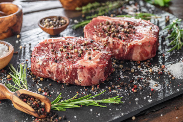 istock Raw Ribeye steaks with salt and herbs on grey board. Top view. 1345260786