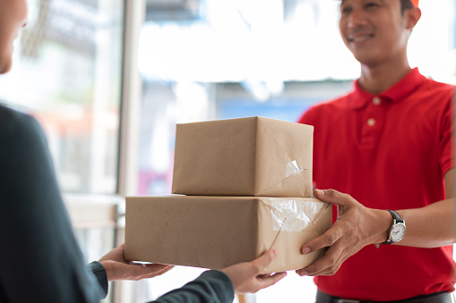 Woman accepting parcel from hands delivery man in red shirt at the door.