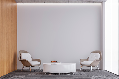 Modern office interior with a lounge corner - a round white glossy table and two comfort chairs in front of a large illuminated empty white plaster, partly hardwood wall background with copy space on carpet floor and large windows on a side. 3D rendered image.