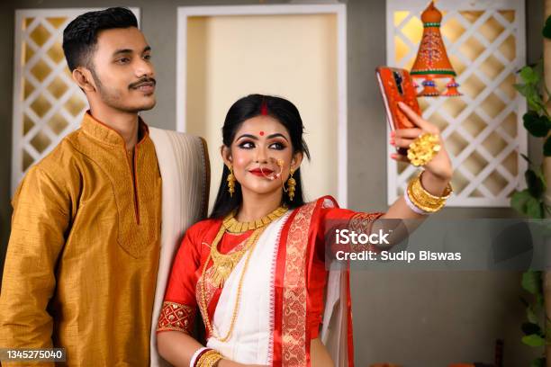 Portrait Of Indian Men Dressed In Kurta Pajama With Beautiful Indian Woman Wearing Traditional Indian Saree Gold Jewellery And Bangles Holding Mobile Phone Taking Selfie Photo Using Smartphone Stock Photo - Download Image Now
