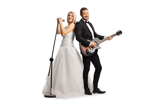 Full length shot of a bride and groom with a guitar and a microphone isolated on white background