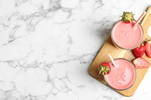 istock Tasty strawberry smoothies in glasses on white marble table, top view. Space for text 1345278667