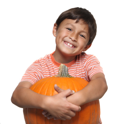 Young boy smiling while wrapping his arms around a large pumpkin on white background with copy space
