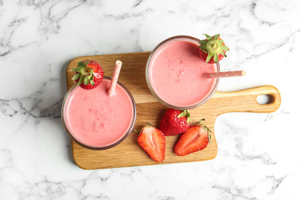 istock Tasty strawberry smoothies in glasses on white marble table, top view 1345282396