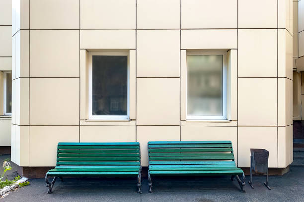 istock Empty bench against classical facade with large white windows in backyard of building. Close-up. 1345284573