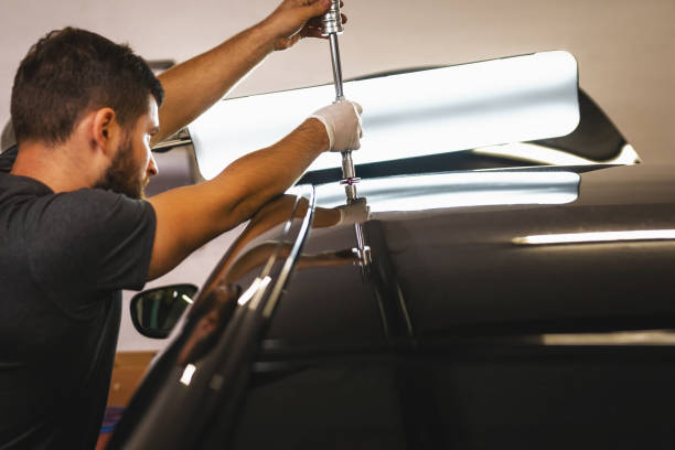 foto de cerca de un mecánico con guantes de protección en proceso de eliminación de abolladuras del techo del automóvil en la estación de servicio. - dented fotografías e imágenes de stock