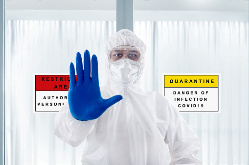 Health worker man with a protective suit and gloves standing with a hand gesture on the hospital