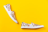 Pair of female's new stylish slip-ons with floral ornament on a yellow background. Flat lay. Copy space. Side view of shoes
