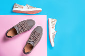Two pairs of a new slip-ons made of floral pattern canvas and sneakers on a pink-blue background. Flat lay. Copy space
