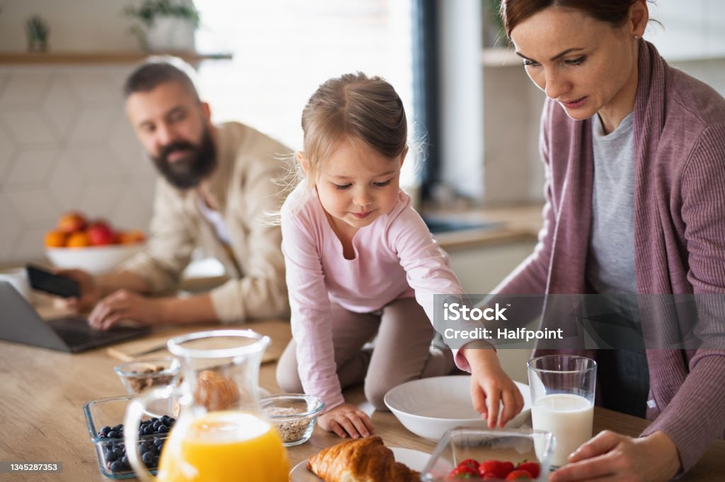 Family with small daughter indoors in kitchen at home, everyday life and home office with child concept. A family with small daughter indoors in kitchen, everyday life and home office with child concept. Morning Stock Photo