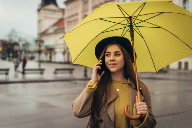 istock Young beautiful woman using a smartphone and holding a yellow umbrella 1345287609