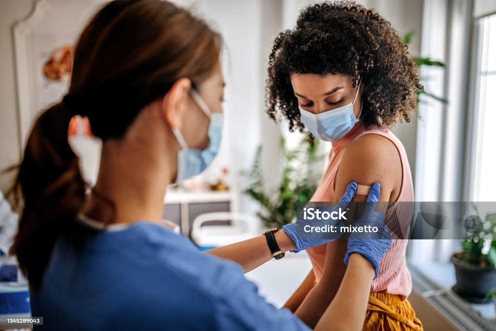 This will all be over in a minute... Photo of nurse putting adhesive bandage on young woman patient’s arm after vaccination at a clinic. Vaccination for covid-19. Vaccination Stock Photo