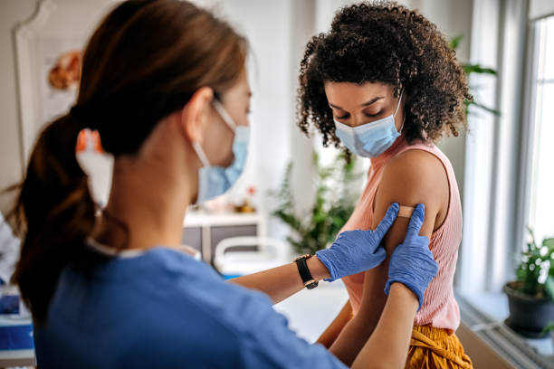 This will all be over in a minute... Photo of nurse putting adhesive bandage on young woman patient’s arm after vaccination at a clinic. Vaccination for covid-19. vaccination stock pictures, royalty-free photos & images