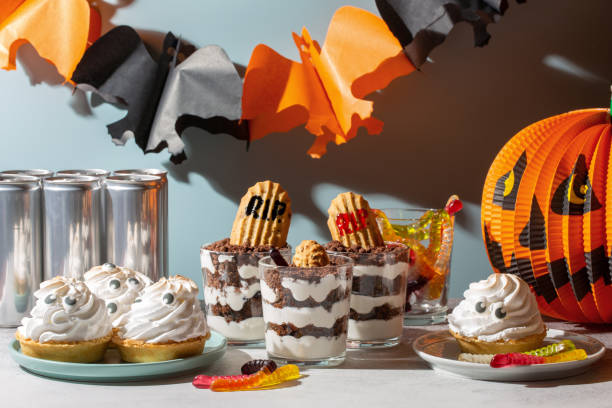 Sweets for Halloween party. Halloween candy buffet. Graveyard trifle  dessert cups,  ghost meringue tarts and scary gummies in Halloween decorations.