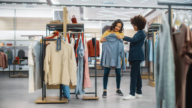 clientes que compran en una tienda de ropa moderna, el asociado de ventas minoristas ayuda al cliente. personas diversas en la tienda de moda, eligiendo ropa elegante, diseños de marcas coloridas, materiales sostenibles de calidad. - fashion store fotografías e imágenes de stock