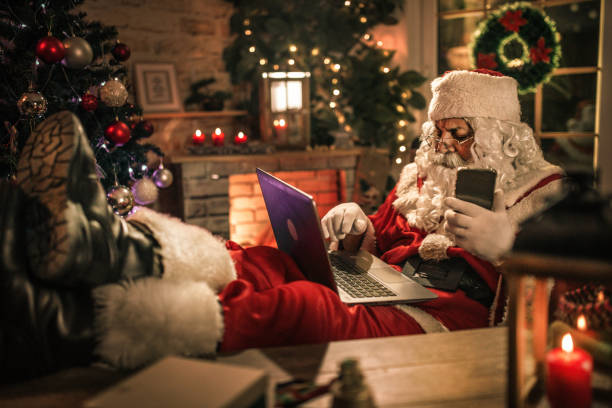 istock happy old Santa Claus using laptop and phone at home 1345293052