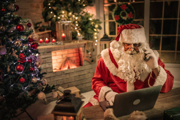istock happy old Santa Claus using laptop and phone at home 1345293488