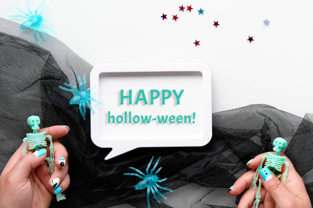 Halloween flat lay with hands and spiders. Text Happy hollow-ween in white frame. Skeletons in hands with Halloween manicure. Flat lay on black mesh with mint green spider decorations Halloween flat lay with hands and spiders. Text Happy hollow-ween in speech bubble frame. Skeletons in hands with Halloween manicure. Flat lay on black mesh with mint green spider decorations. weben stock pictures, royalty-free photos & images