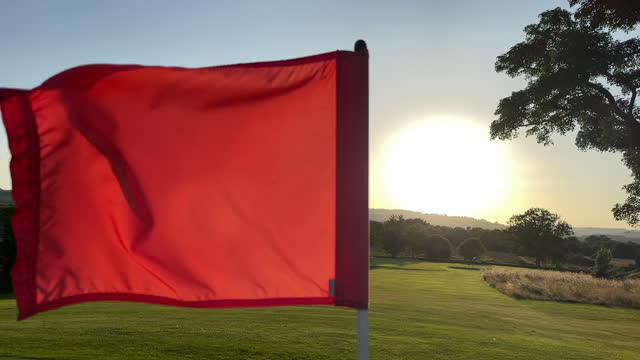 Golf flag blowing in the wind as the sun is setting behind the fairway